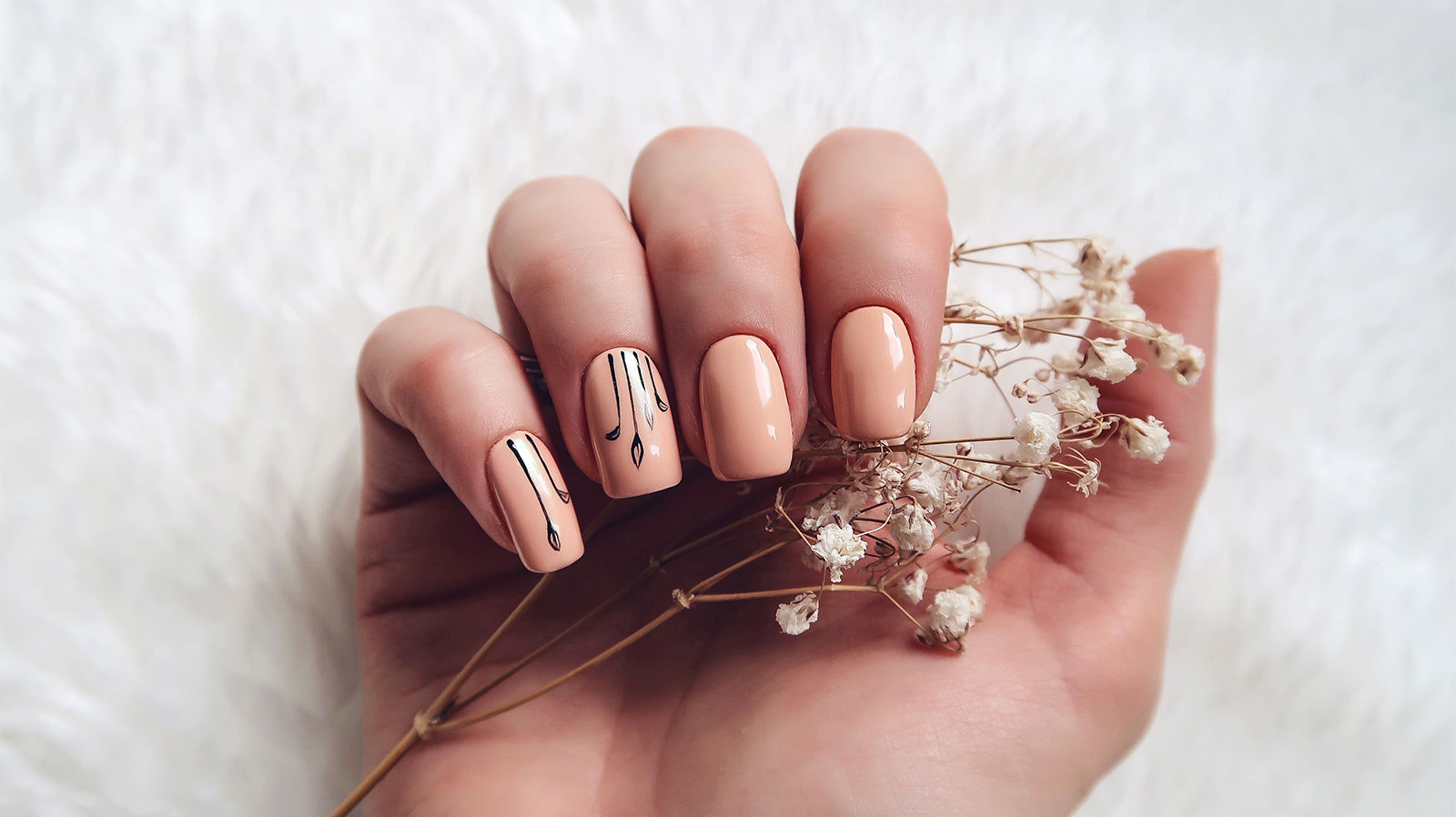 Nude manicure with fine black line art, hand holding dried white flowers