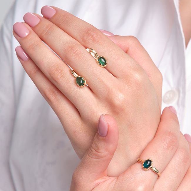 Pale pink manicure on hands wearing emerald and gold jewelry