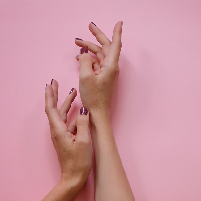 Deep plum glossy nails on hands against a pink backdrop